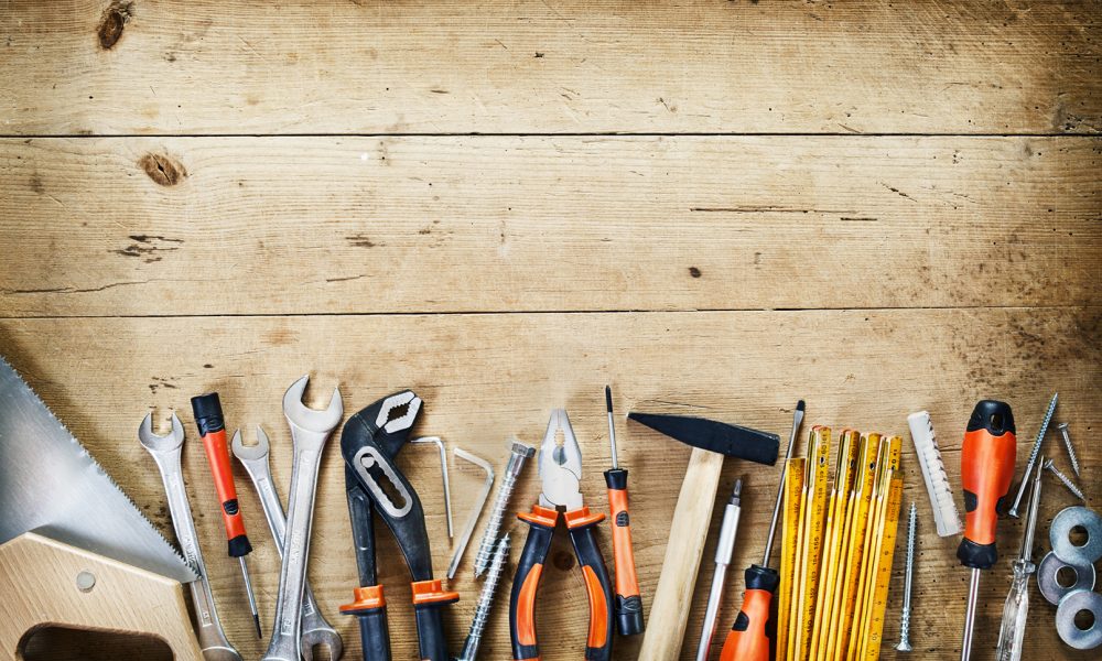 Bottom border of assorted hand tools arranged in a neat row conceptual of DIY, renovations, repair, building and woodworking over wood with copy space and vignette